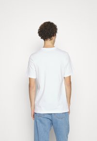 Camiseta blanca de algodón con un cuello redondo clásico, mangas cortas y un corte relajado, combinada con unos jeans de mezclilla azul claro, vista desde la parte posterior.