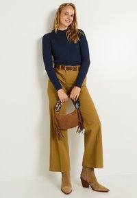 Haut long à manches longues côtelé bleu marine, pantalon large taille haute moutarde, ceinture marron, bottes à talons en suède marron, et sac à main marron avec des franges.
