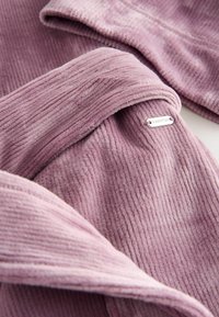 Pehme lilla kangas, millel on sooniline tekstuur. Omab volditud disaini ja väikest hõbedast sildi kangale külge.