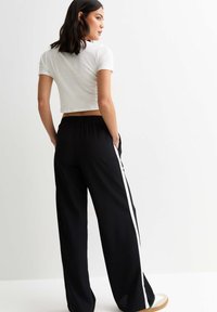 Svarta vidabyxor med vit sidostrand och elastisk midja, i kombination med en figurnära vit kort t-shirt. Slät tygstruktur.