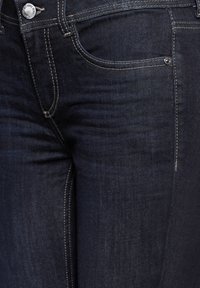 Jeans en denim foncé avec un léger effet décoloré, couture renforcée, design classique à cinq poches et fermeture à bouton en métal à la taille.