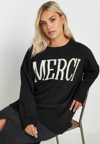 Svart stickad tröja med en krämfärgad "MERCI" grafik. Långa ärmar med ribbade muddarna och nederkanten, som ger en avslappnad passform.
