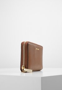 Brun læderpung med en struktureret overflade, guld lynlås langs den ene side, rektangulær form og præget logo på forsiden.