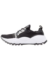 Svartvitt atletiskt träningsskor med nätövredel, tjock vit sula, svarta snörningar och dragflik vid hälen, sidovy.