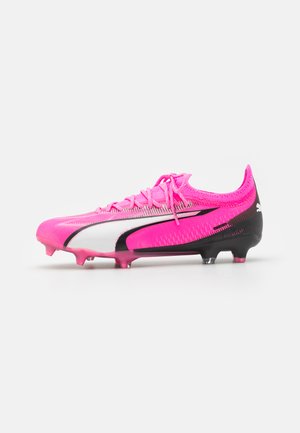 Scarpe da calcio con parte superiore rosa, dettagli bianchi e neri, superficie testurizzata e tacchetti rotondi per una migliore trazione sulla suola.