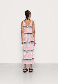 Stickad maxiklänning i rosa med grön och svart zigzag-mönster, med V-back och en luftig silhuett. Matcherad med svarta sandaler.