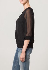 Svart blus med genomskinliga långa ärmar, smockad midja och rund halsringning. Matchad med åtsittande blå jeans.