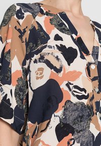 Blusa floreale in tessuto morbido, con scollo a V, dettaglio con bottoni e motivo astratto in tonalità di blu navy, beige e pesca.