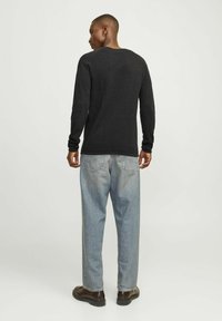 Maglietta nera a maglia a maniche lunghe, vista posteriore, abbinata a jeans in denim azzurro chiaro. Presenta un collo rotondo e polsini aderenti, design semplice.