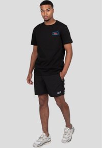 Camiseta de algodón negra de manga corta, con un parche de logotipo colorido. Combinada con pantalones cortos negros, ambos con un corte relajado y sin patrones.