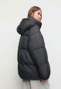 Giacca a petto nera con design trapuntato, cappuccio e vestibilità ampia. Presenta polsini elasticizzati e una superficie liscia e lucida.