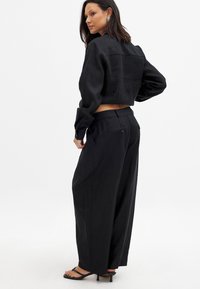 Črna skrajšana majica s rahlo teksturiranim zaključkom, kombinirana z širokimi črnimi hlačami. Hlače imajo zadnje žepe in diskretne gumbe.