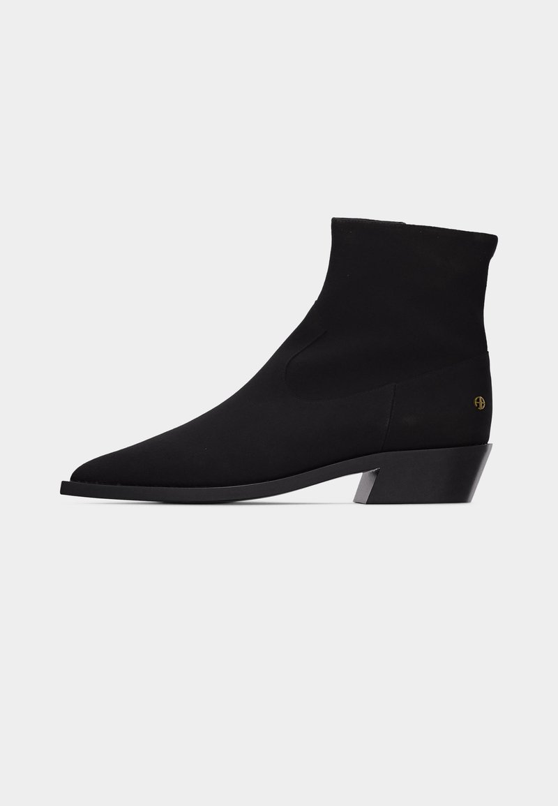 Black mid-calf pointed toe boot with low angled heel and small gold logo near heel on plain light gray background.