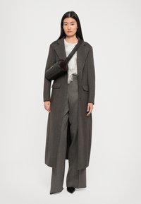 Gray long coat over a white, feather-textured top and plaid, wide-leg trousers. A round, brown crossbody bag completes the look.