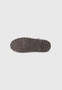 Suela de bota de goma marrón con un dibujo profundo para tracción, que presenta un patrón de zigzag y un logo rectangular cerca del talón.