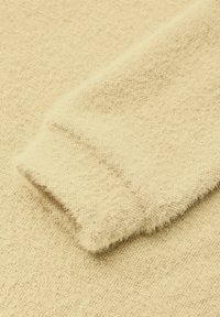Tessuto di maglione beige a maglia con una superficie morbida e testurizzata e un polsino ripiegato caratterizzato da una finitura sottile e pelosa.