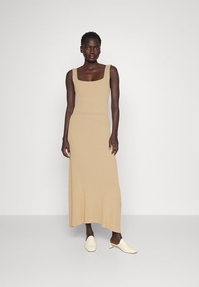 Vestido largo de punto acanalado en beige con escote cuadrado. Complementado con mules de punta cuadrada color crema, exhibido sobre un fondo neutro.