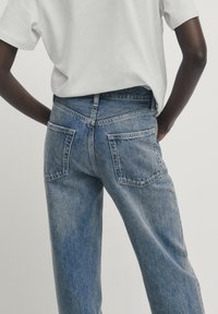 Ljusblå denimjeans med avslappnad passform, hög midja, bakfickor och blekt textur. Kombinerade med en vit t-shirt.