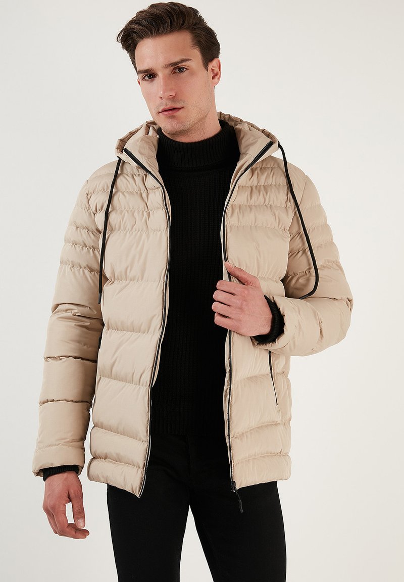 Bežs pūkains jakas ar rāvējslēdzēju priekšpusē, kapuci un melniem auklām. Iezīmējas ar quilted struktūru un elastīgām aprocēm, stilizēts virs melnas džemperis.