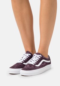 Sneaker in suede viola con lacci bianchi e strisce laterali, caratterizzati da un design low-top e tessuto testurizzato. Suole in gomma leggere.