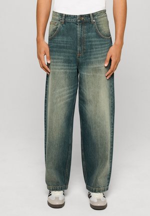 Džínsy s širokými nohavicami v bledomodrom vypratom dizajne, obsahujúce päť vreciek, zapínanie na gombík a kontrastné prešívanie, doplnené bielymi teniskami.