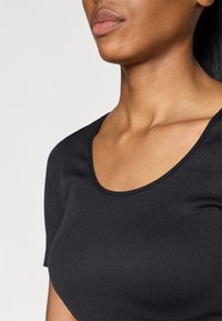Black ribbed short-sleeve top featuring a scoop neckline, smooth texture, and fitted silhouette, showcasing subtle stretch and shaping.
