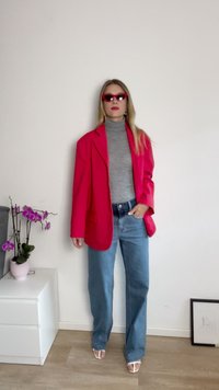 Roter übergroßer Blazer, grauer Rollkragenpullover, hellblaue weit geschnittene Jeans und weiße Sandalen mit offenem Zehenbereich. Die Accessoires umfassen rote Katzenaugen-Sonnenbrillen.
