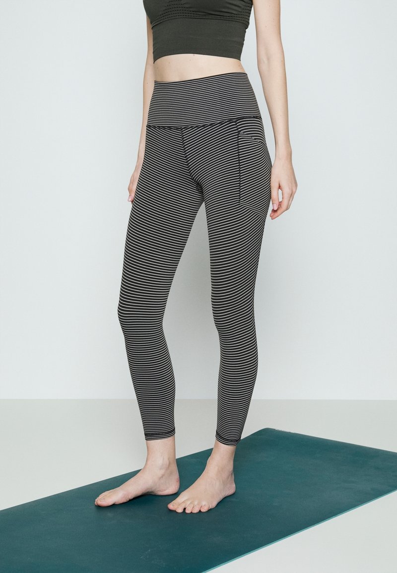 Leggings à rayures noires et blanches avec une large taille élastique et une poche latérale. Le matériau semble extensible, ajusté et lisse au toucher.