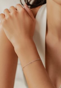 Silver bracelet with delicate chain design, featuring small circular accents, placed on a tan wrist, with smooth skin texture.