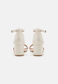 Hælte sandaler i glanset off-white laklæder med justerbare ankelremme og blokhæl. Åben tå-design med minimale detaljer.