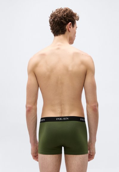 Άνδρας, ο οποίος φαίνεται από πίσω, φοράει εσώρουχα τύπου μποξεράκια σε ελαιόχρωμο με μαύρη ζώνη μέσης με την ετικέτα «POLO RALPH LAUREN» σε απλό ανοιχτόχρωμο φόντο.