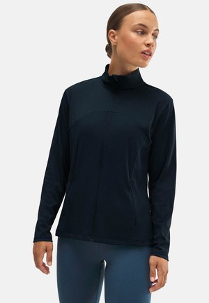 Chaqueta atlética de color marino con cremallera frontal, cuello alto y mangas largas. Presenta una textura suave y un diseño ajustado con bolsillos laterales.