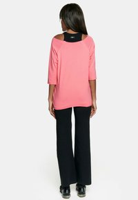 Różowa bluzka z rękawami o długości trzy czwarte i okrągłym dekoltem, w połączeniu z czarnymi spodniami dzwonami. Bluzka ma luźny krój i odsłania strefę ramion.