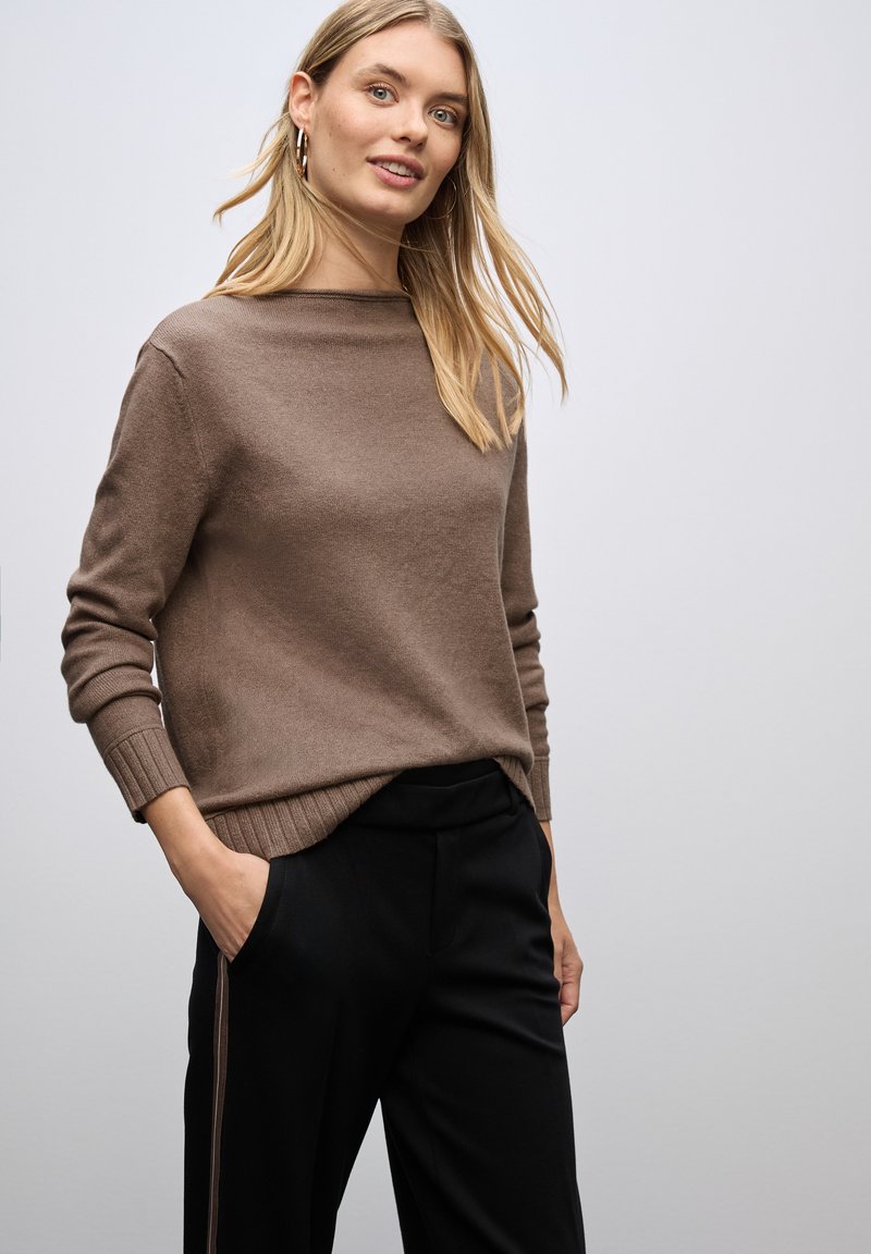 Brauner Strickpullover mit Rundhalsausschnitt, gerippten Bündchen und Saum, kombiniert mit schwarzen Hosen, die einen Seitenstreifen haben.