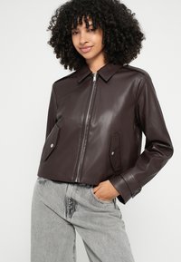 Brūna ādas cropped jaka ar apkakli, rāvējslēdzēja aizdari un sānu kabatām. Teksturēts virsējais slānis ar piegriezta izskatu.