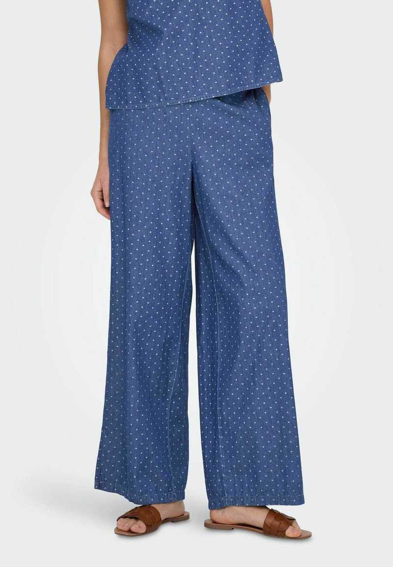 Dżinsowy komplecik składający się z luźnej bluzki i szerokich spodni, oba w niebieskie kropki na białym tle. Materiał wydaje się lekki i teksturowany.