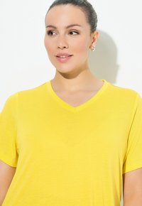 T-shirt giallo a maniche corte con scollo a V, realizzato in tessuto morbido, caratterizzato da un design semplice e una vestibilità comoda.