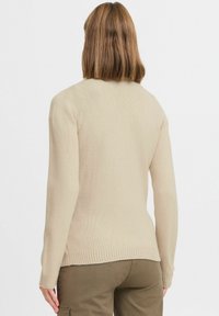 Beige gestrickter Pullover mit langen Ärmeln und einem gerippten Saum. Der Rücken hat eine glatte Textur und eine figurbetonte Silhouette. Keine Verzierungen.