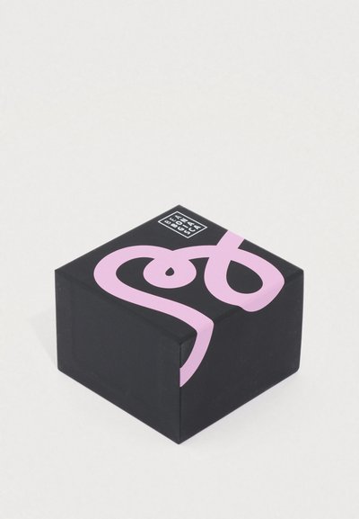 Μαύρο τετράγωνο κουτί με στρογγυλεμένες άκρες, με έντονο ροζ αφαιρετικό σχέδιο και μικρό λογότυπο στην κορυφή. Ομαλή ματ υφή.