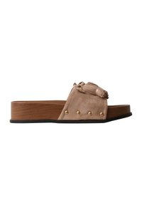 Sandale mule en daim beige avec semelle plateforme en bois, clous dorés et un détail décoratif à pompon sur la bride supérieure.