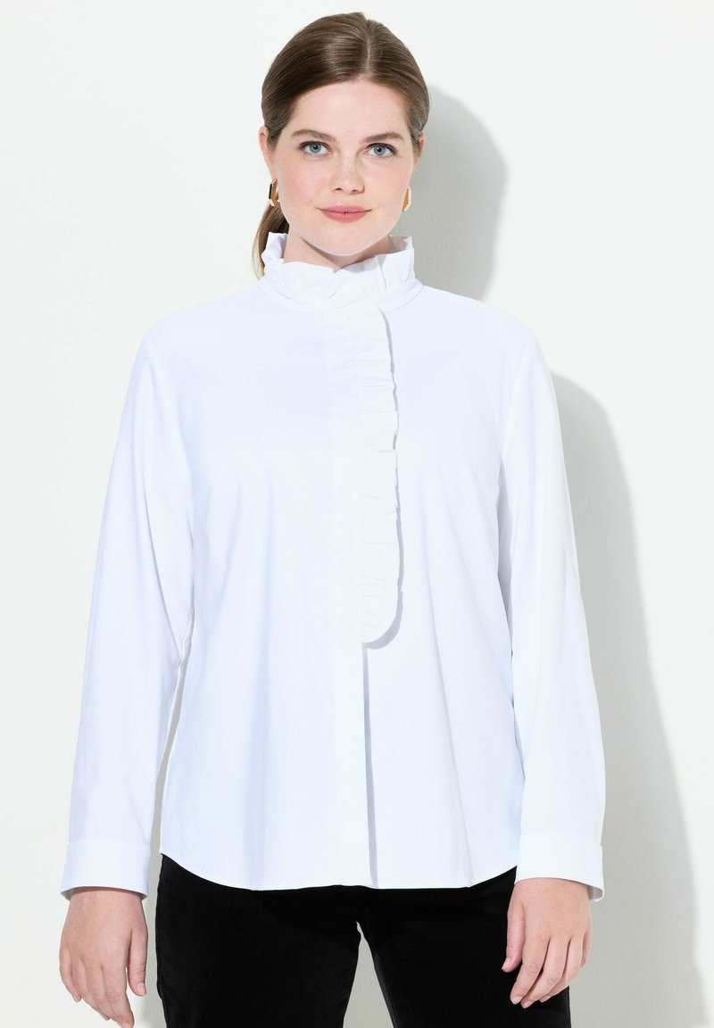 Camicia bianca a maniche lunghe con colletto alto e dettagli arricciati sul davanti. Tessuto morbido con vestibilità rilassata e chiusura con bottoni.