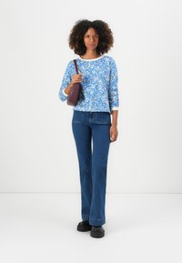 Blå och vit mönstrad långärmad topp i kombination med högmidjade blå jeans och svarta platåskor, håller en vinröd handväska.