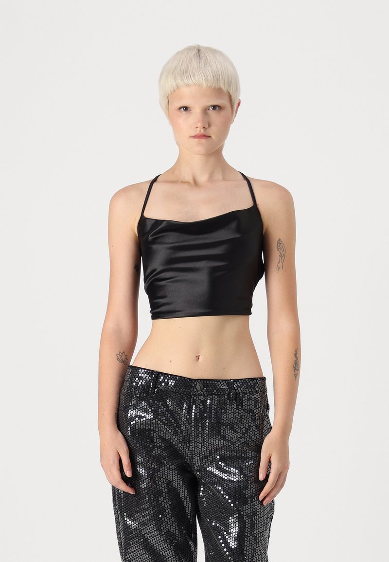 Fekete szatén crop top, ívelt kivágással és vékony pántokkal, fényes fekete flitteres nadrággal párosítva, sima és elegáns megjelenést teremtve.