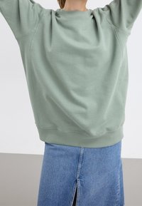 Lichtgroene sweatshirt met een ronde halslijn en ribgebreide manchetten, gecombineerd met een blauwe jeansrok met een split aan de voorkant. Zachte textuur, ontspannen pasvorm.