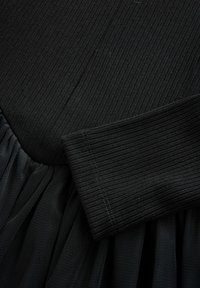 Schwarzes Kleid mit geripptem Oberteil und Tüllrock. Der Stoff ist weich mit einer glatten Textur und erzeugt einen mehrlagigen Look.