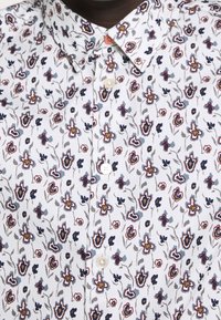 Košile s krátkým rukávem vyrobená z lehkého materiálu, s bílým základem a vícebarevnými květinovými vzory, má špičatý límec.