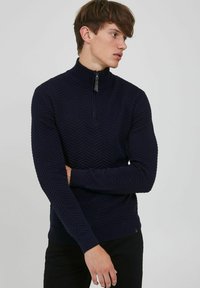 Maglione con colletto zip di colore blu navy con un motivo a zigzag testurizzato, caratterizzato da maniche lunghe e polsini e orlo a costine. Tessuto a maglia comodo.