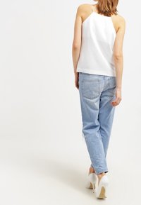 Top bianco senza maniche con taglio dritto; abbinato a jeans azzurri chiari e ampi; indossando tacchi alti bianchi. Nessun motivo particolare osservato.