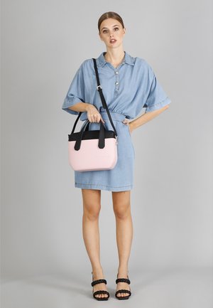 Rosa und schwarze Handtasche mit glatter Textur, abgerundeter Form und zwei Griffen. Kombiniert mit einem hellen Jeanskleid und schwarzen Sandalen mit Riemchen.