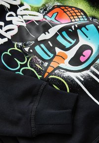Sweatshirt noir avec un graphique coloré d'un bonhomme de neige portant des lunettes de soleil et un nez en carotte. Poignets côtelés et accents de couleurs vives.